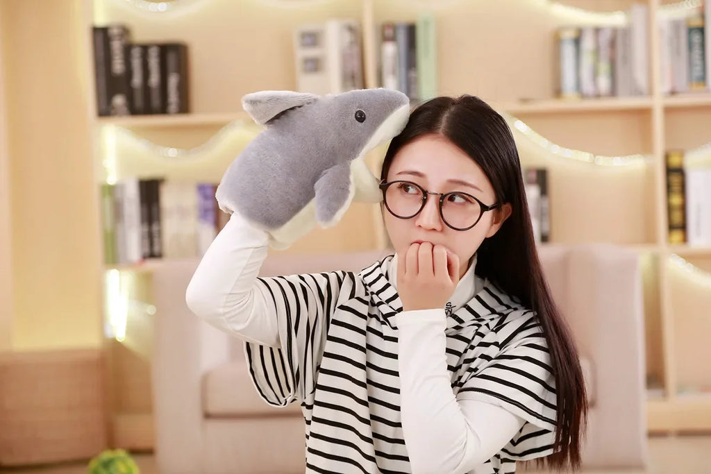 Woman holding a plush shark toy in a room with bookshelves.
